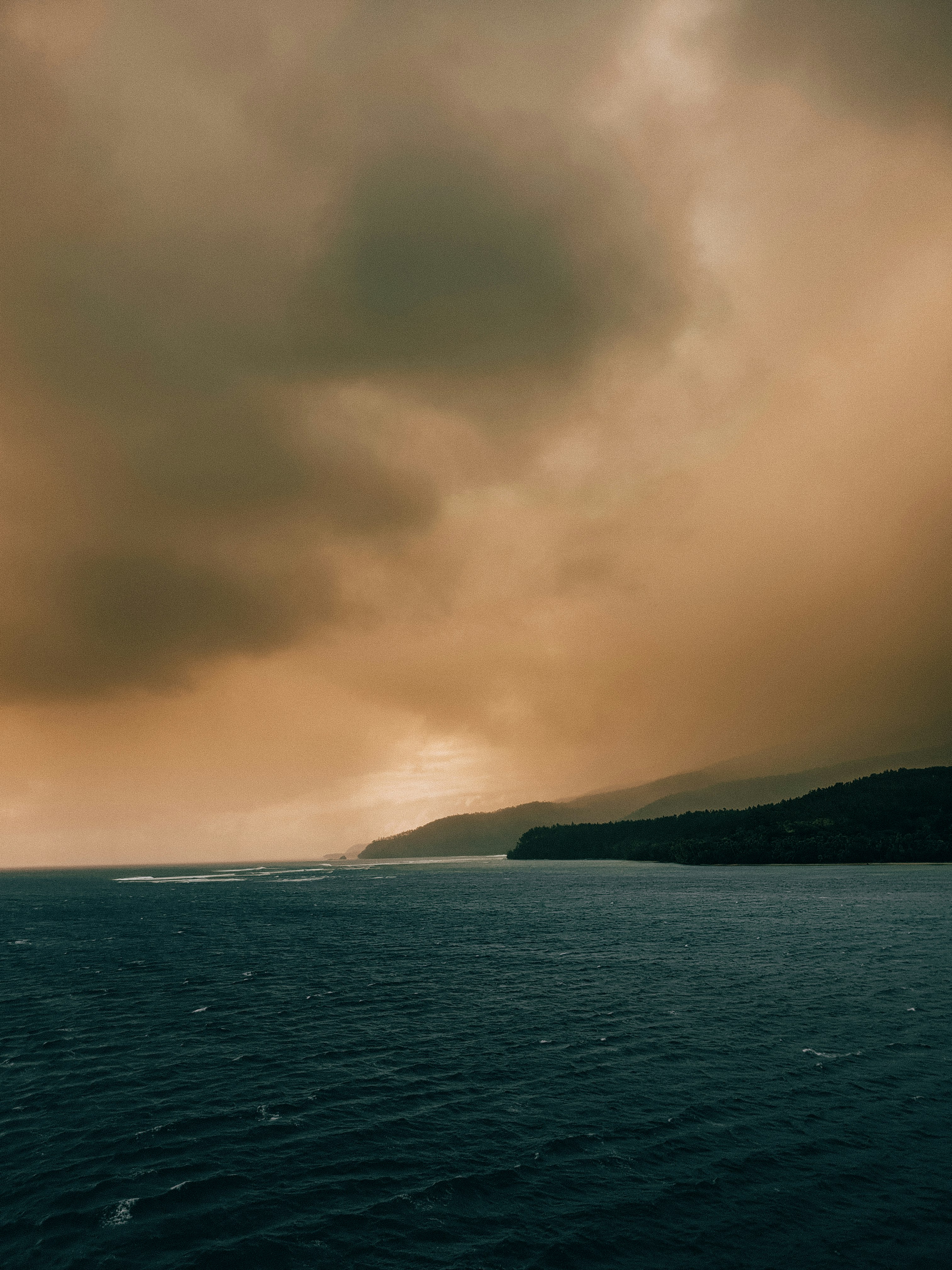 body of water near mountain under cloudy sky during daytime